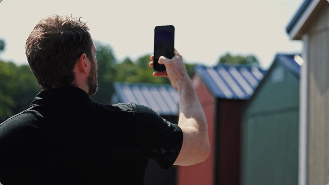 A Liberty Sheds salesperson photographing a shed on the lot with a phone