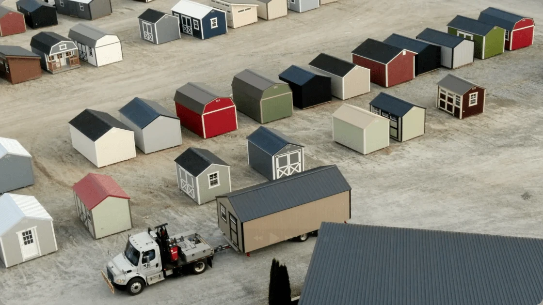 Finished sheds lined up on the Westwood Sheds lot, with a delivery truck loading